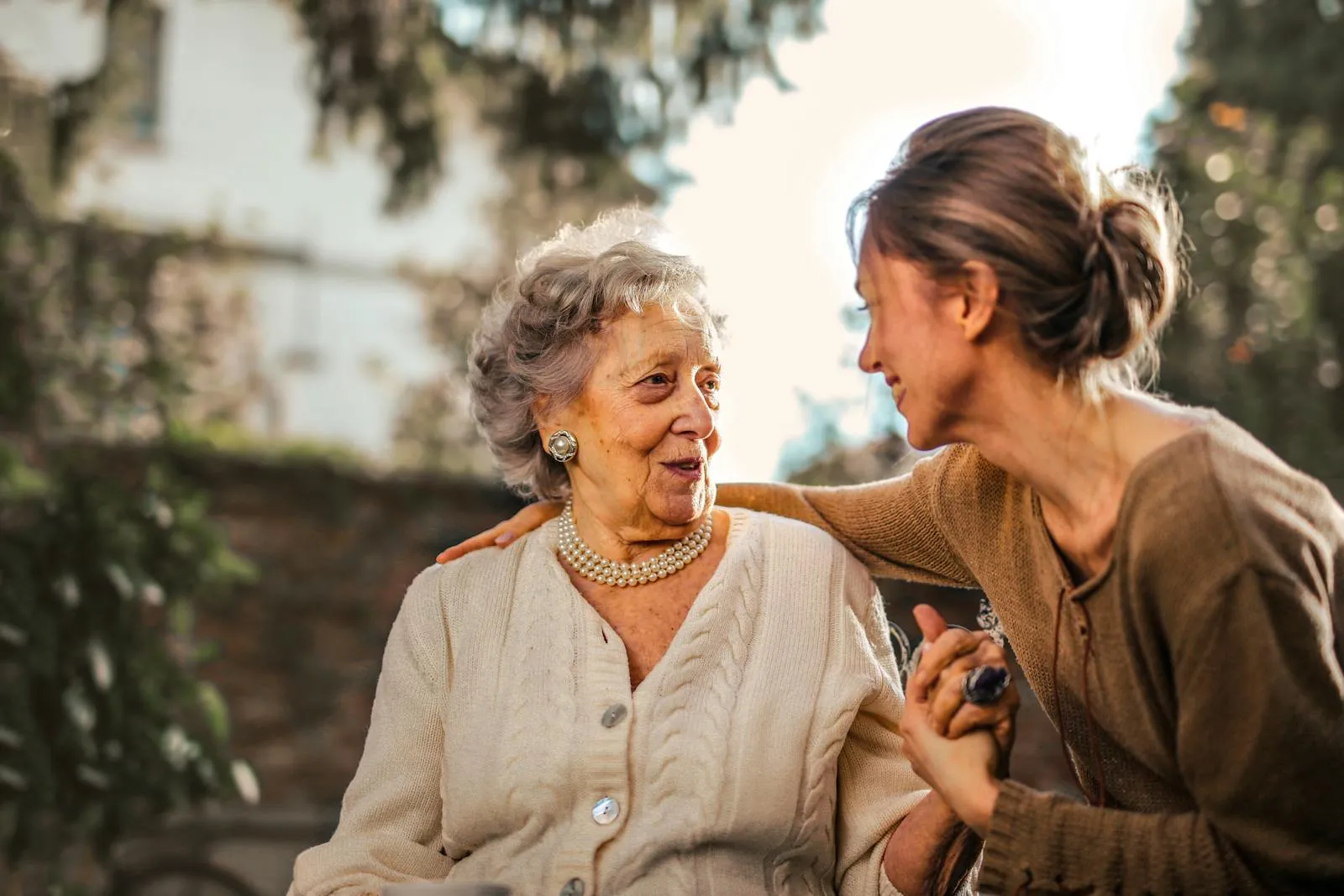 A caregiver with her arm around a smiling older woman, outdoors